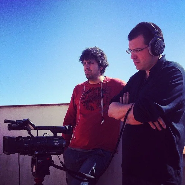 Guillem Barceló and Gerard Pastor wearing headphones, checking the viewfinder of a video camera during a shoot.