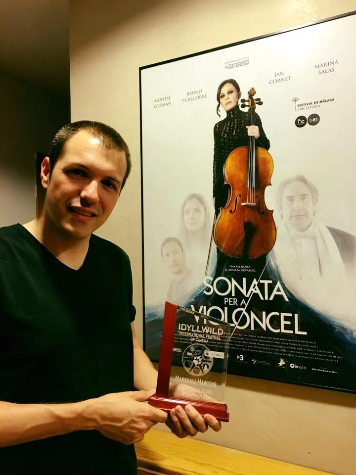 Gerard Pastor holding the award from the Idyllwild Film Festival with the poster of the film Sonata for Cello in the background.