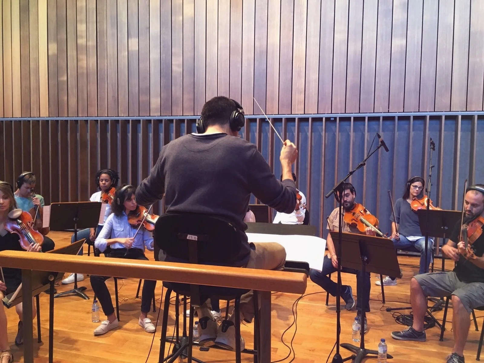 Gerard Pastor from behind, conducting the Furius Music Orchestra during a recording session in a wood-panelled auditorium.